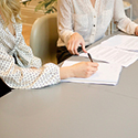 Image of two women sitting next to each other at a table with paperwork in front of them