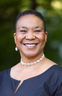 Image of a woman with short, dark hair, wearing a dark shirt and white necklace. She is smiling