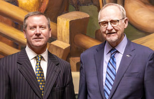 Two white men wearing suits and ties standing next to each other.