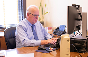 Image of Milt Nuzum behind his desk typing on his keyboard computer.