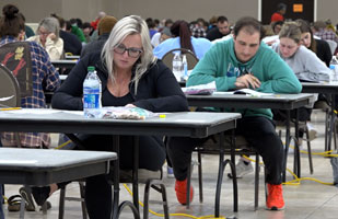 Image showing men and women deep in thought and concentration as they take the Ohio Bar Exam seated at tables in a large room.