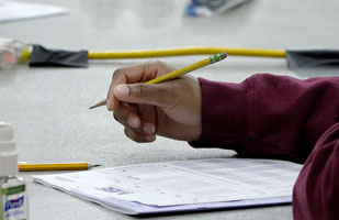 Image of a hand holding a pencil over a stack of test papers.