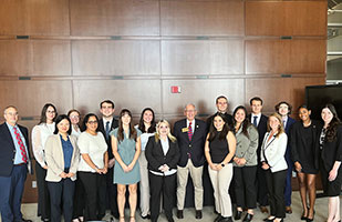 Image of several men and women standing in front of a wood panel wall.