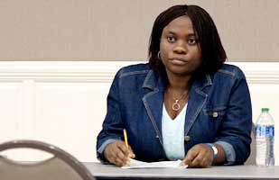 Image of a woman wearing a blue jean jacket and white top sitting at a table with a pencil in her hand.