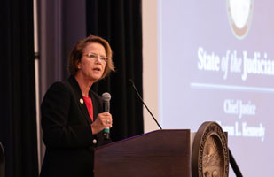 Image of a woman wearing a black suit and red blouse speaking from a wooden podium.