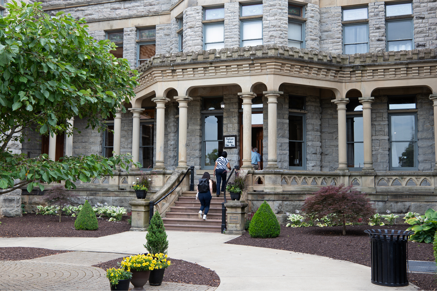 People enter a large, stone building with pillars.