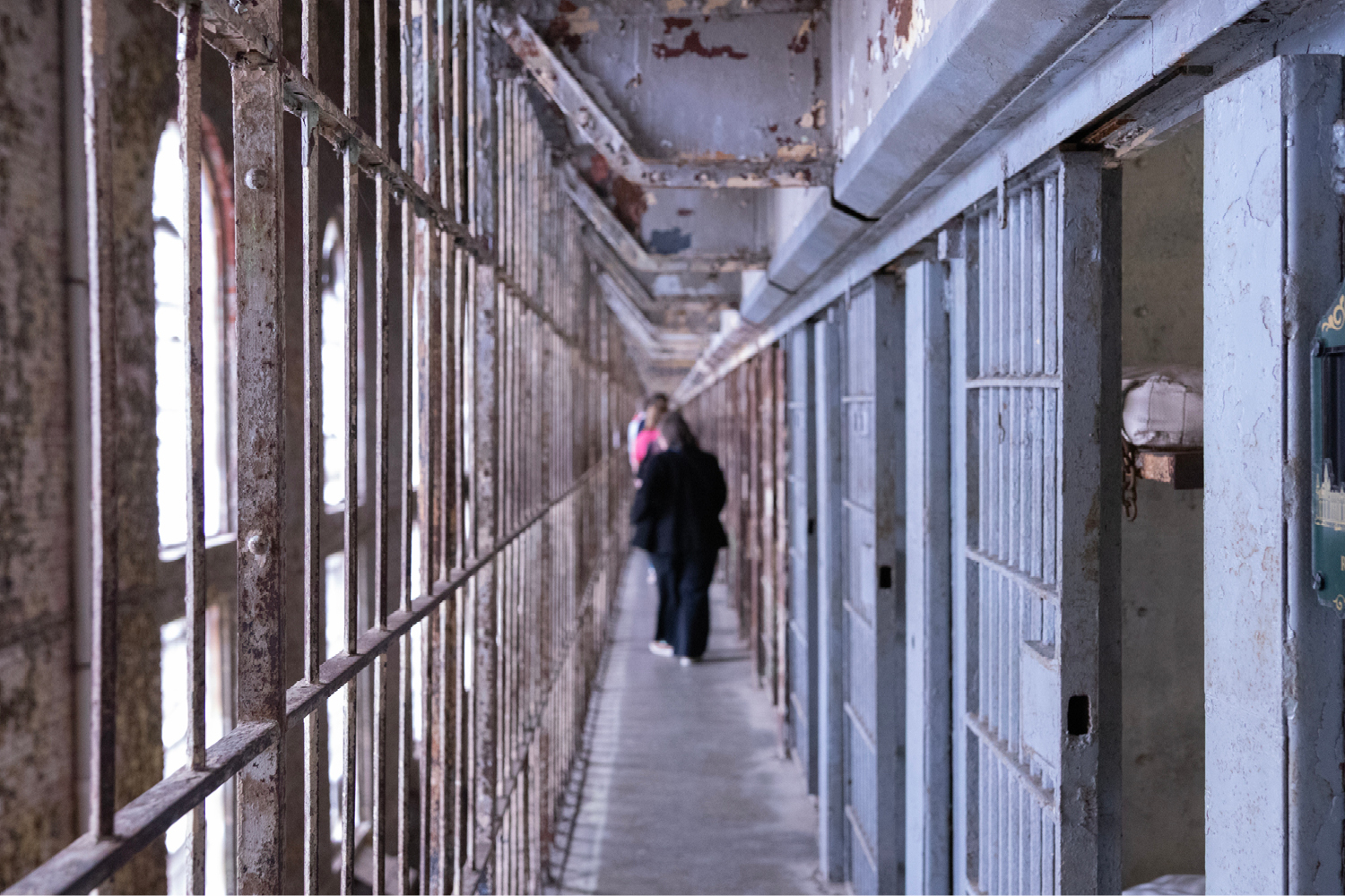 People walk the narrow corridor outside a row of prison cells.