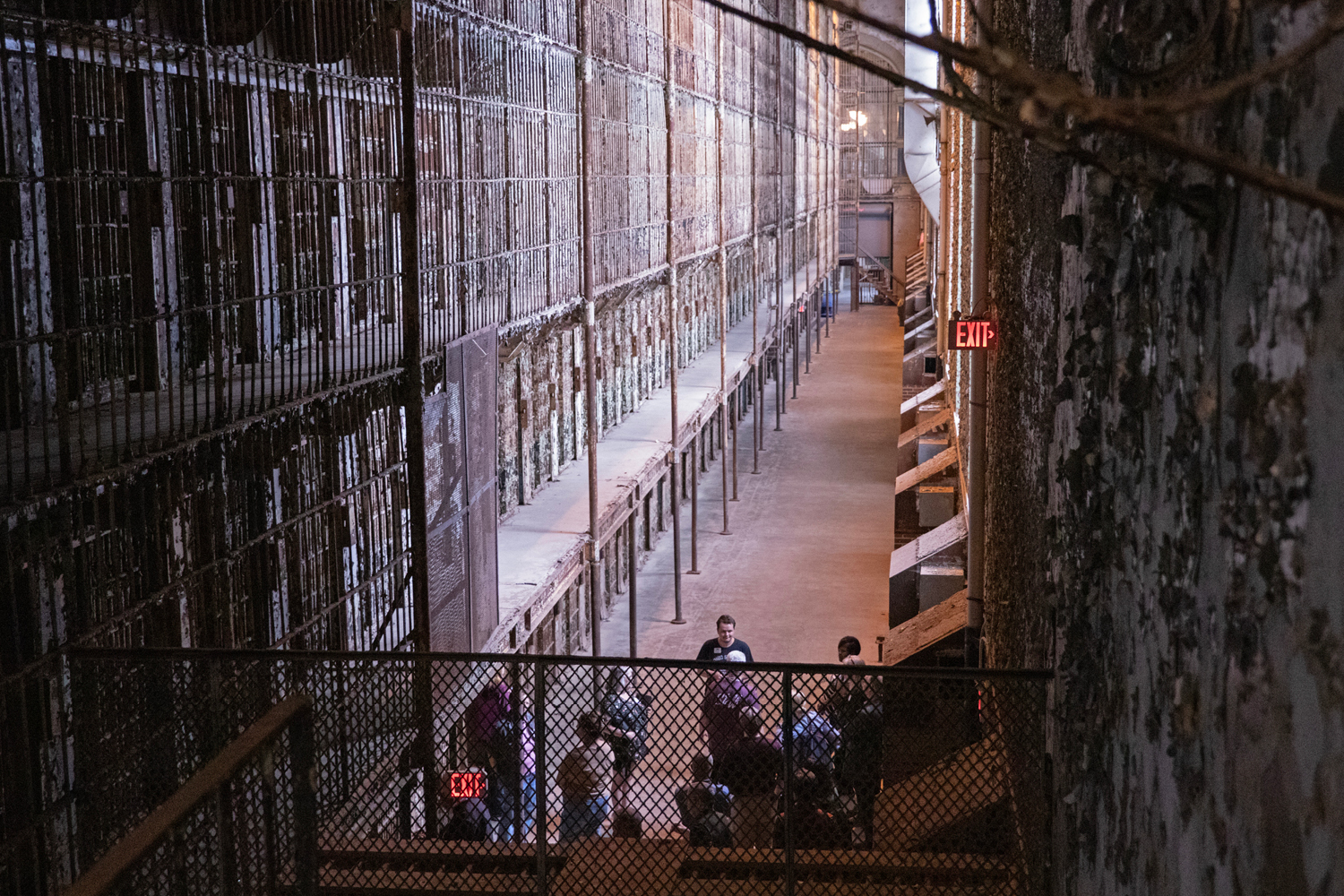 A group of people gather in front of a multi-level wall of prison cells.