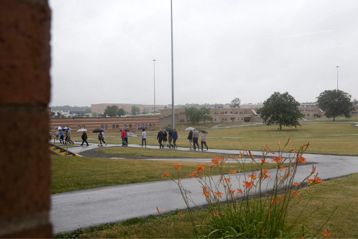 A group of men and women, some holding umbrellas, walk down a sidewalk.
