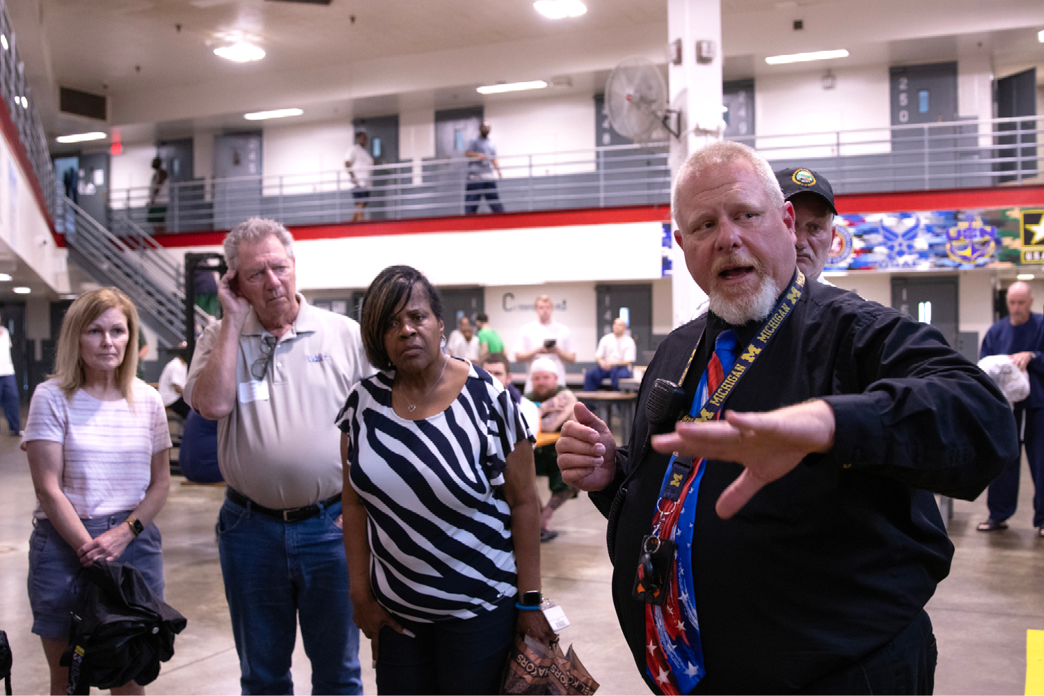two women and a man stand next to a mean wearing a black dress shirt and a red, white, and blue tie in a prison common area.