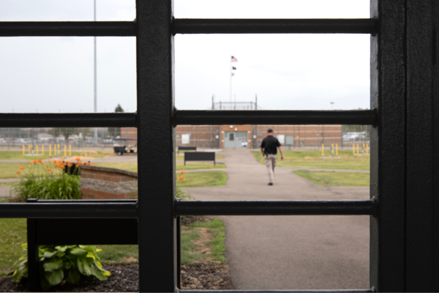 A man walking down a sidewalk as seen through a window with metal bars on it.