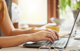 Image of a woman's hands typing on a laptop keyboard.