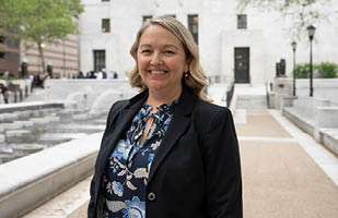 A woman wearing a flower print blouse and black blazer standing next to a reflecting pool.