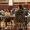 A large group of women and men sitting at tables with laptops.