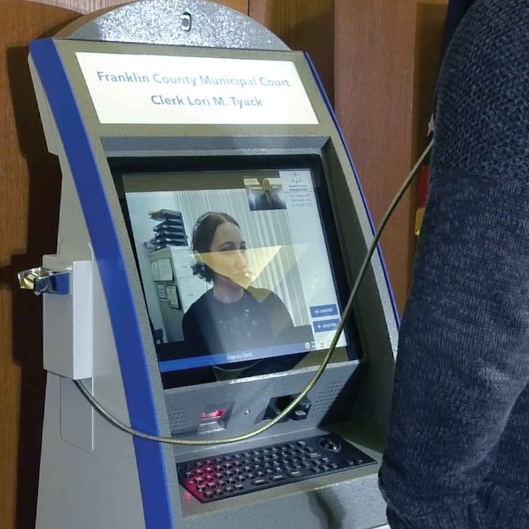 An interactive kiosk with a person talking on the attached phone to a woman on the screen