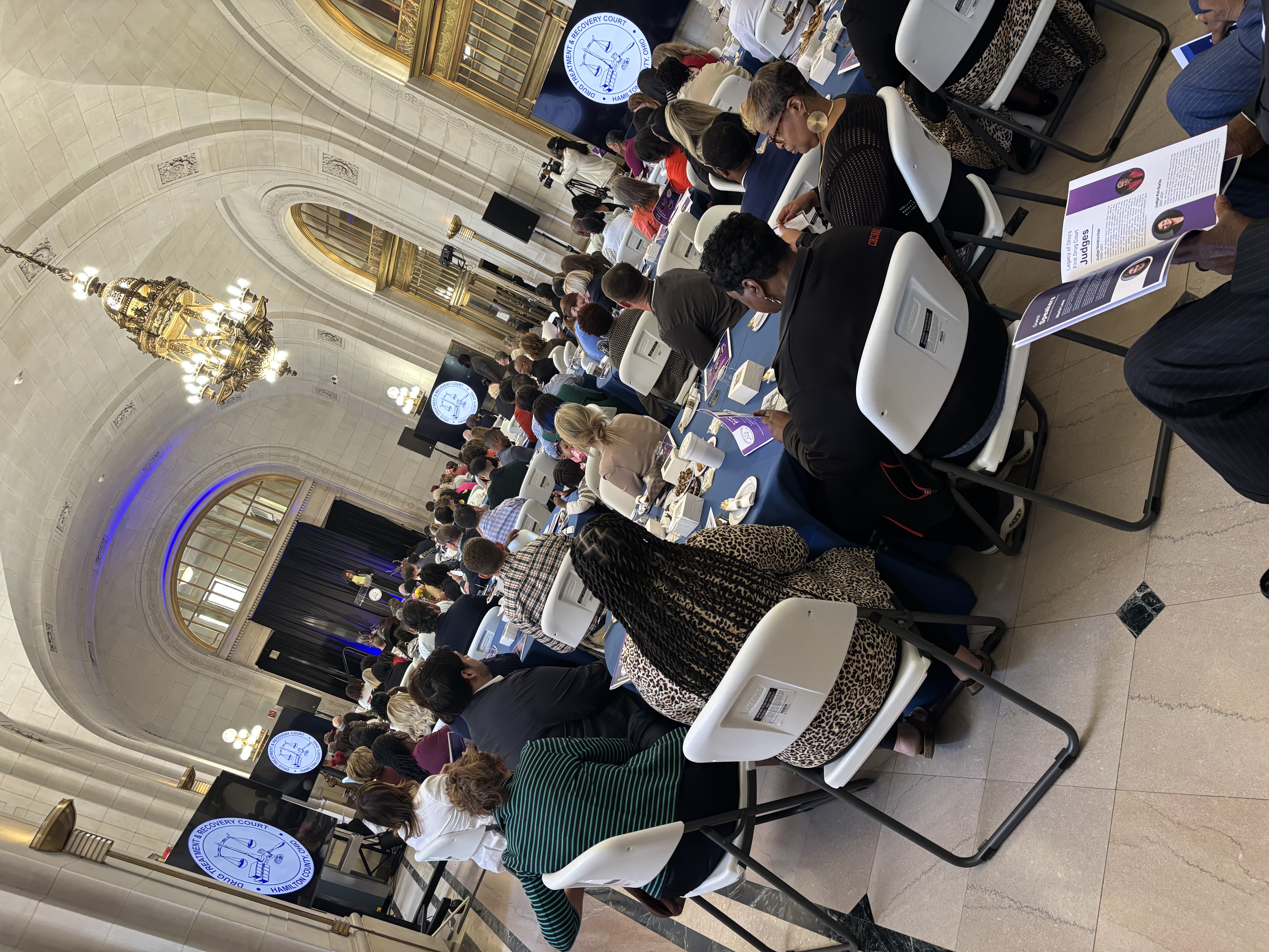 A group of men and women listen to a speaker talk while sitting at round tables