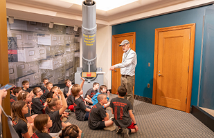 A male tour guide showing a group of children a cannon with text that reads the shot heard around ohio