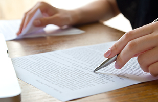 A hand holding a pen resting on a printed document.