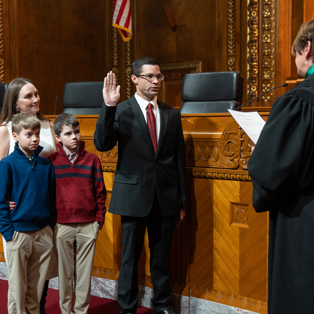 Person in a suit taking an oath in a courtroom, standing beside family while Chief Justice reads from oath
