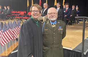 A man wearing an Army uniform and a woman wearing a judicial robe smiling