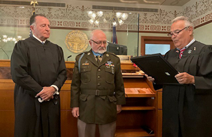 Two men in judicial robes giving an award to a man in an Army uniform
