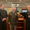 Two men in judicial robes giving an award to a man in an Army uniform