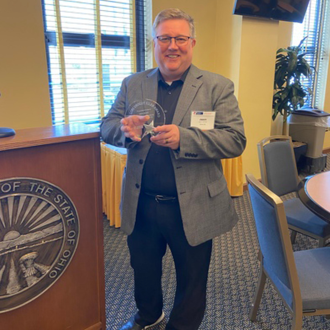 A man smiling holding a glass award wearing a suit