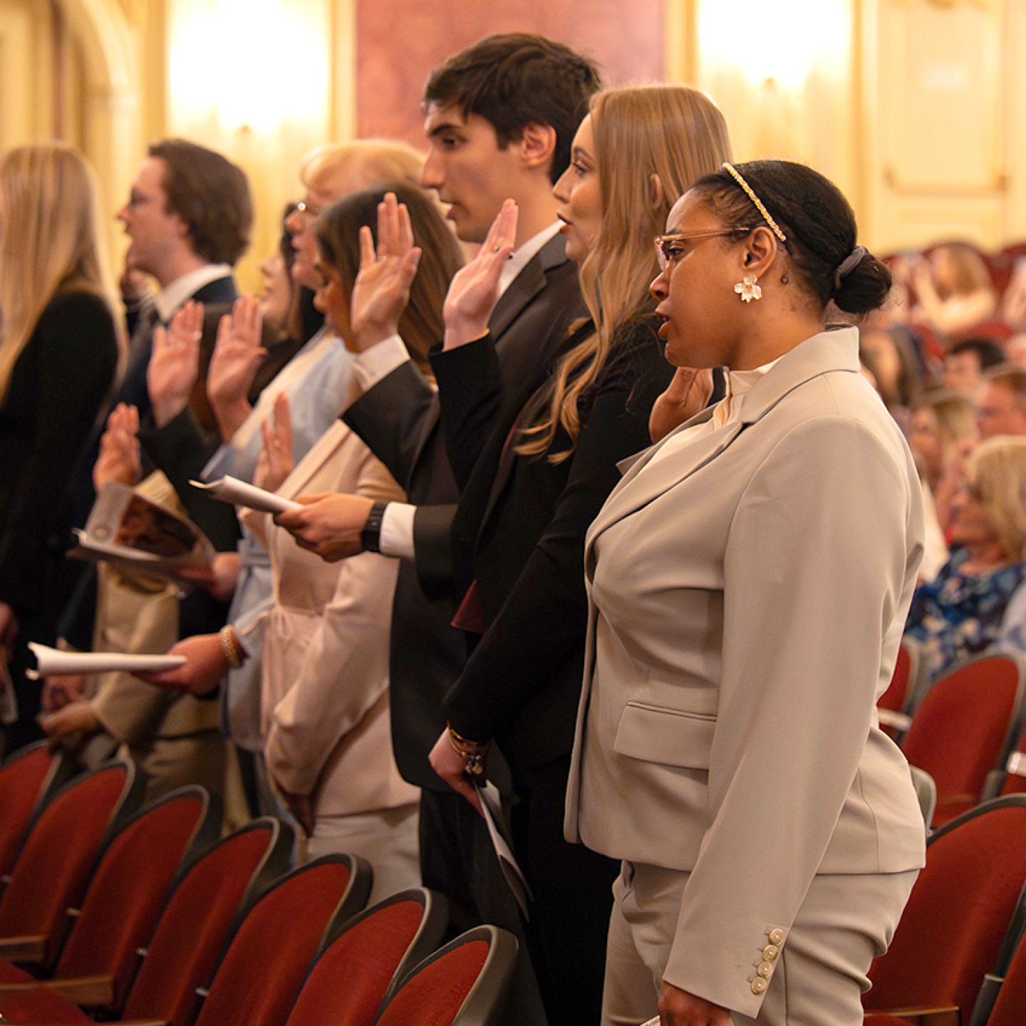 A group of people in formal attire raise their right hands, during a ceremony.