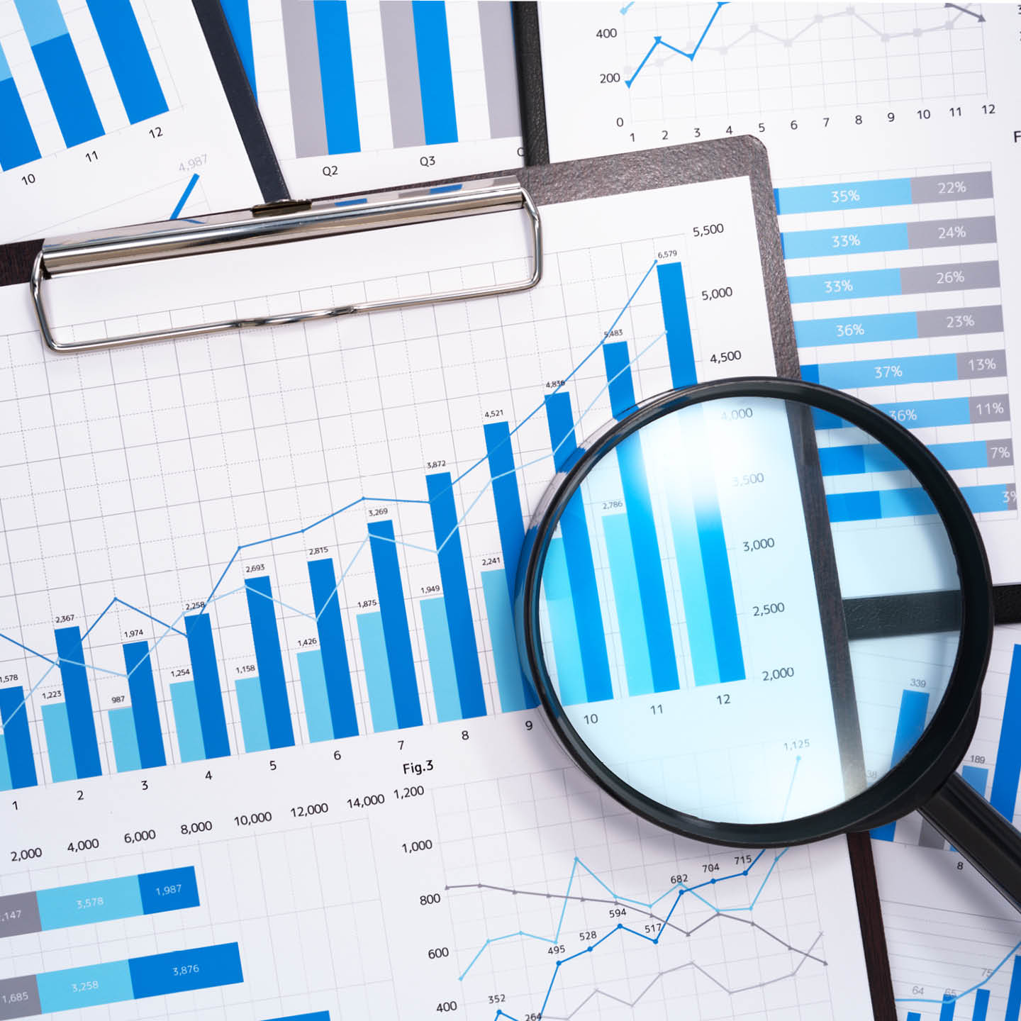 Various blue bar and line graphs on paper, depicting data and trends, with a magnifying glass emphasizing analysis.
