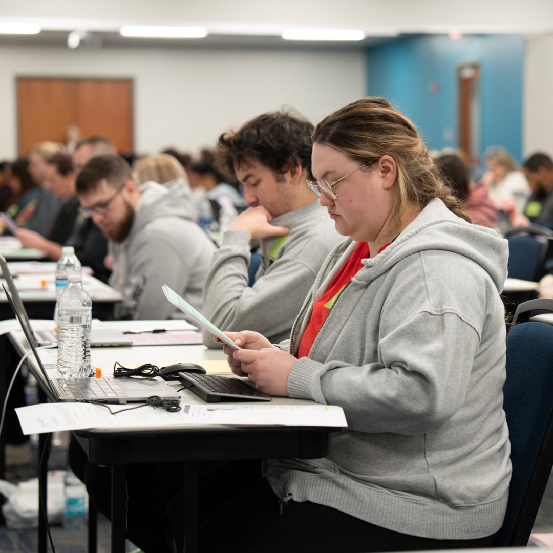 A room full of students reading papers and looking at laptops