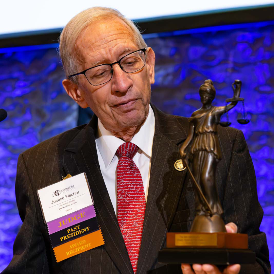 An elderly man in a suit and red tie admires a Lady Justice statue.
