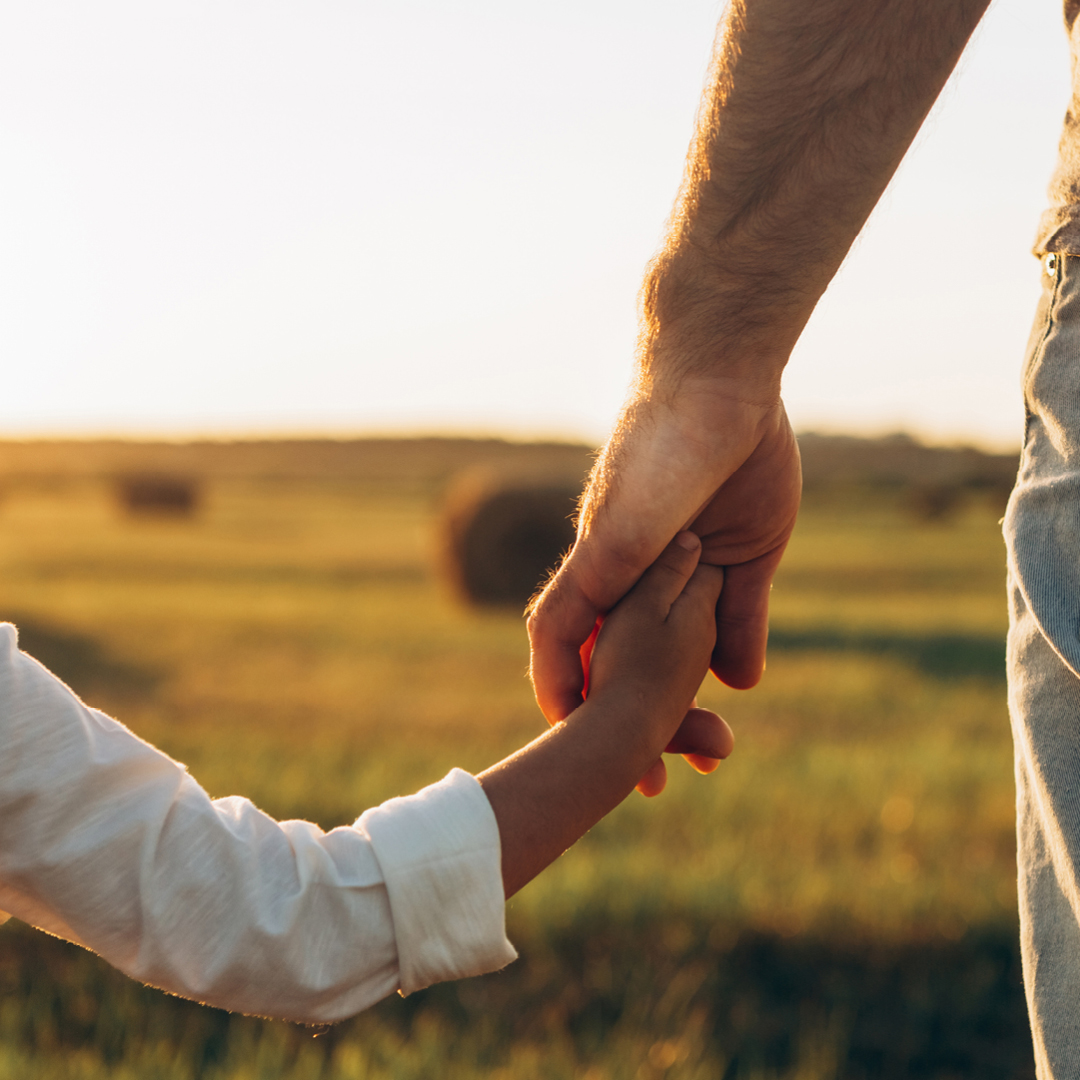 A parent and child holding hands walking into a sunset