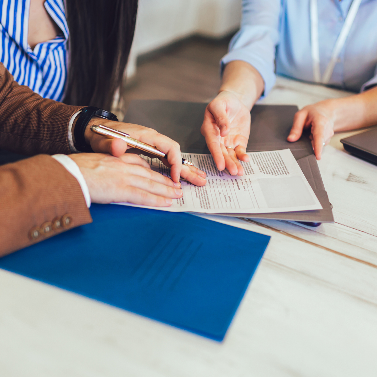 People review and sign a printed document beside a blue folder on a table.