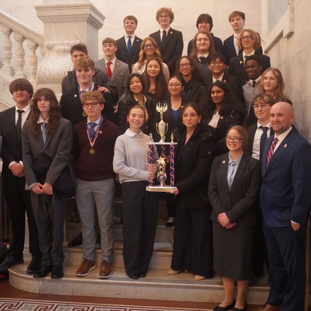 A group of 24 teens and two teachers smiling with a trophy