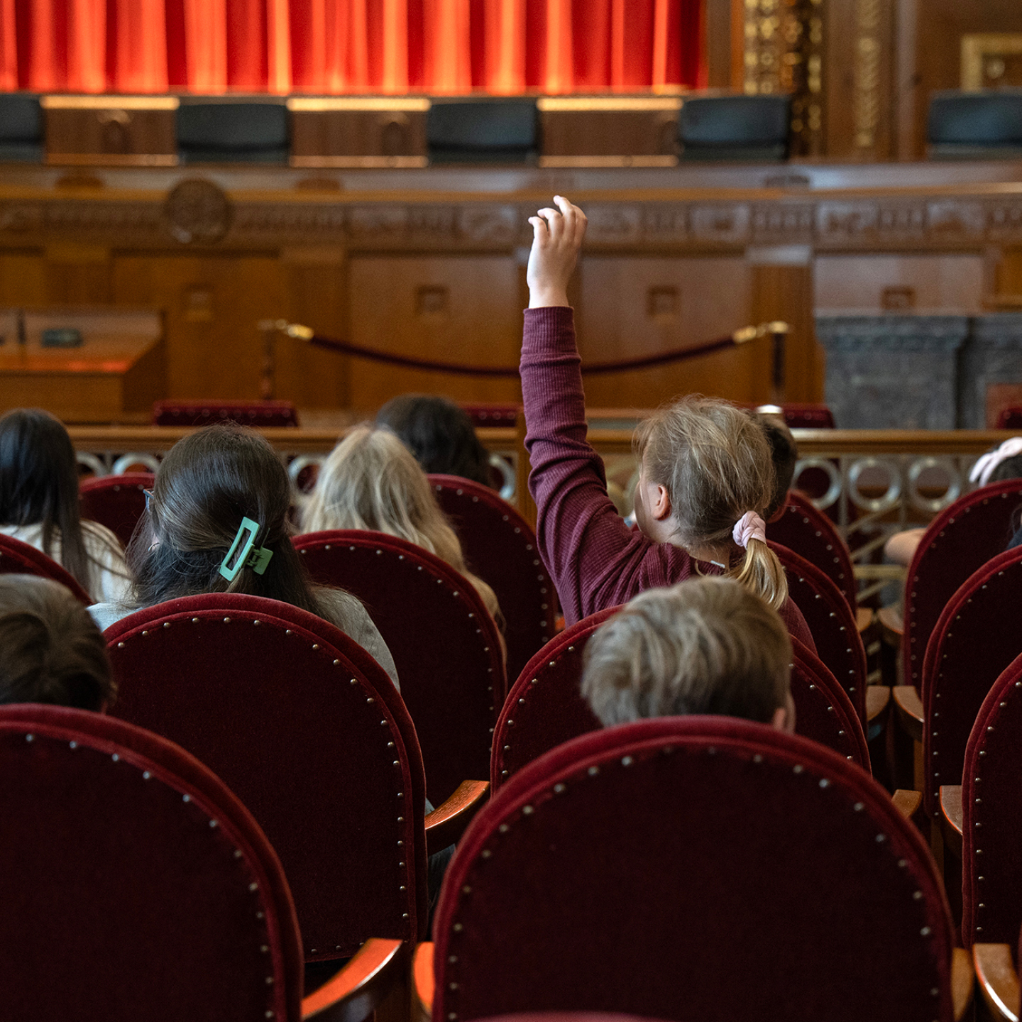 A student rasing their hand in a room with other students watching a tour guide