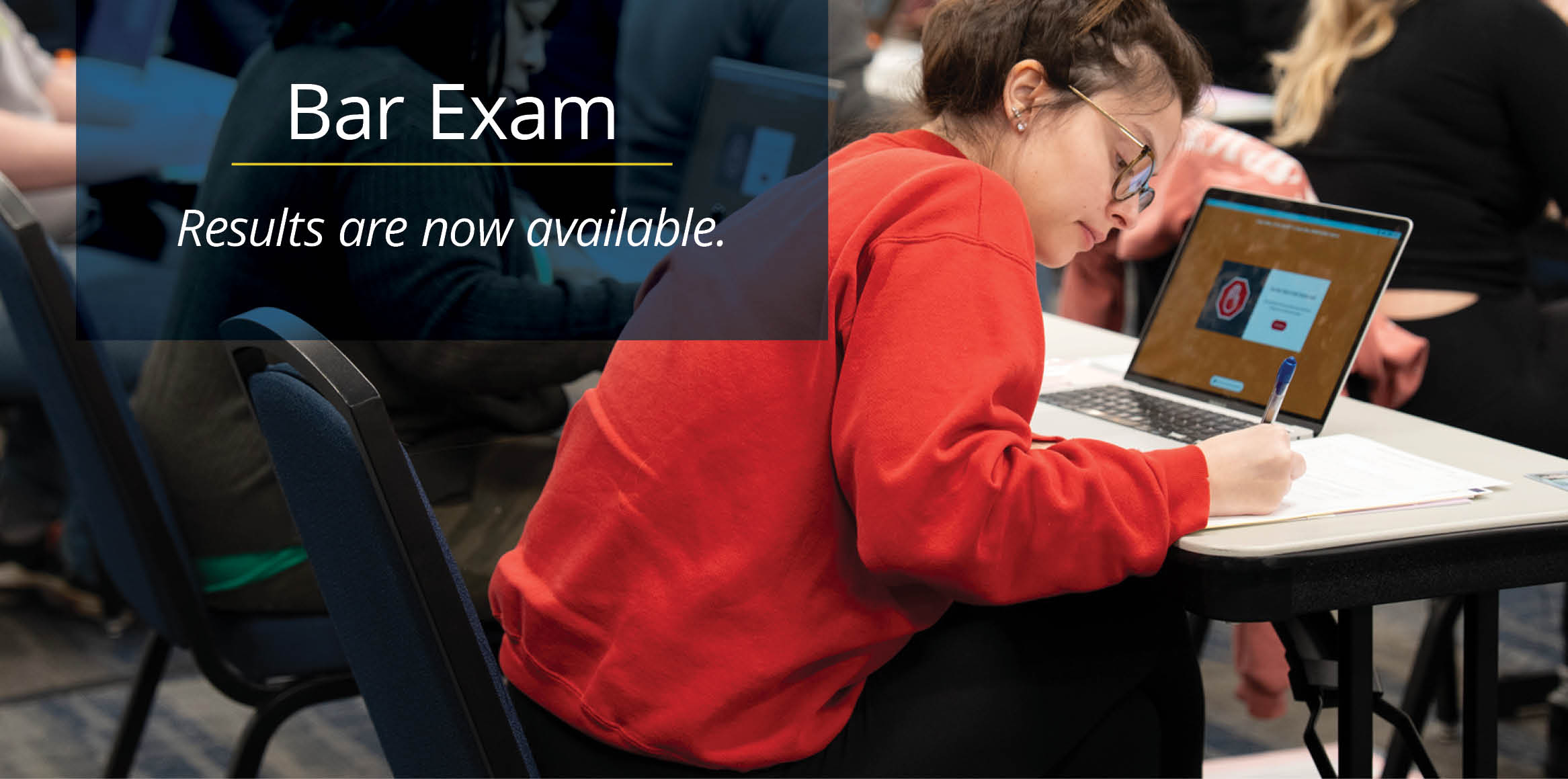 Student writing beside a laptop in a classroom, overlaid with the message 'Bar Exam: Results are now available.'