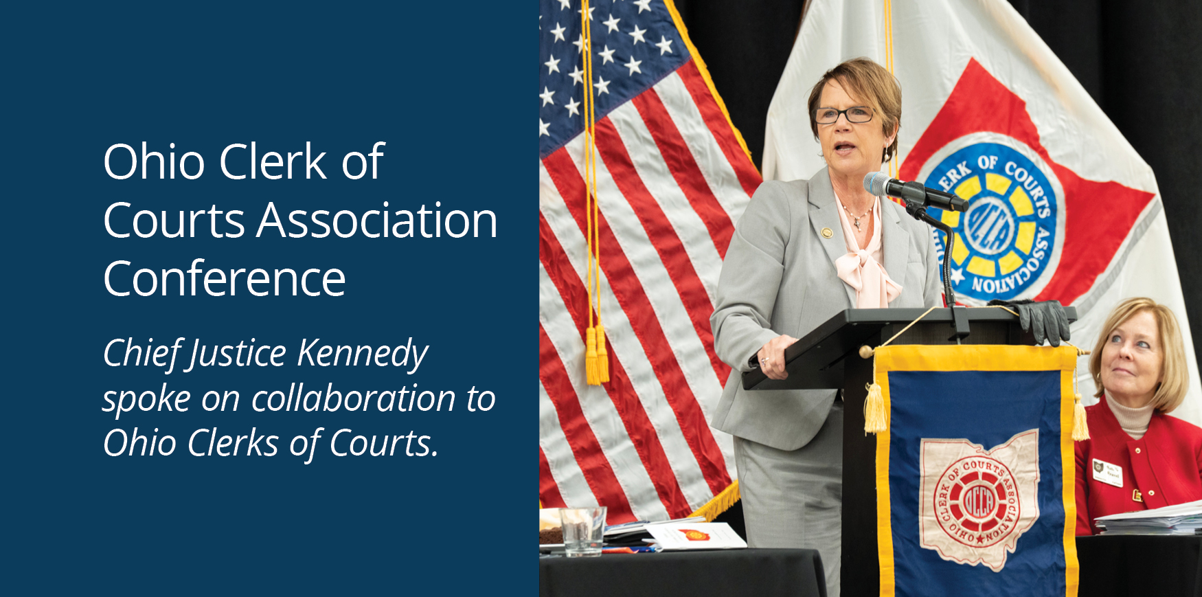 A woman wearing a grey business suit speaking from a podium.