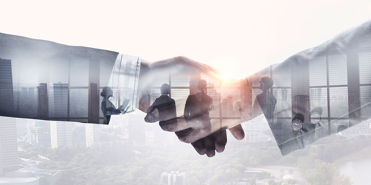 Image of two hands shaking over top of four people looking out of an office window overlooking a downtown city