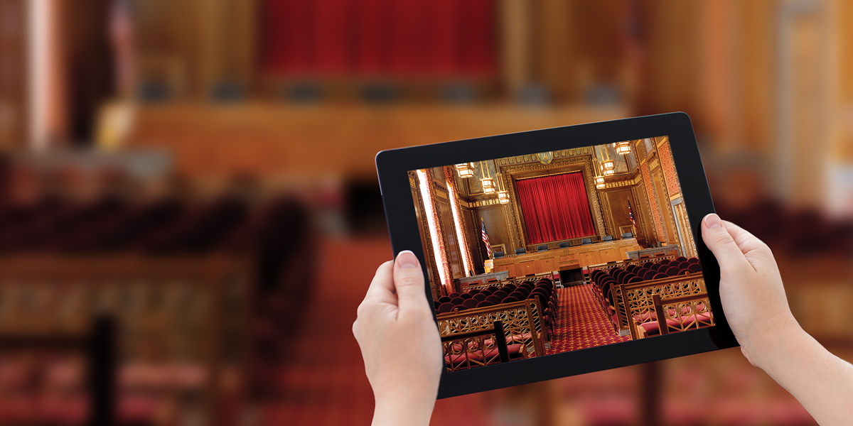 Image of hands holding a tablet showing the courtroom of the Thomas J. Moyer Ohio Judicial Center