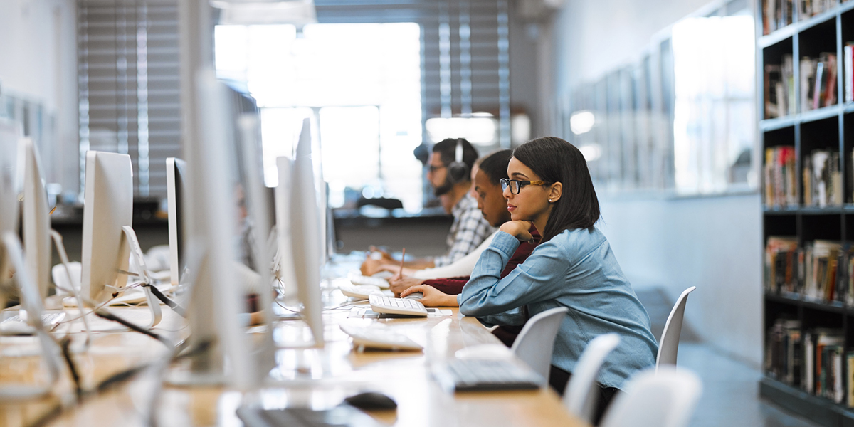 Image showing rows of computers with three people sitting in front of them (iStock/PeopleImages)