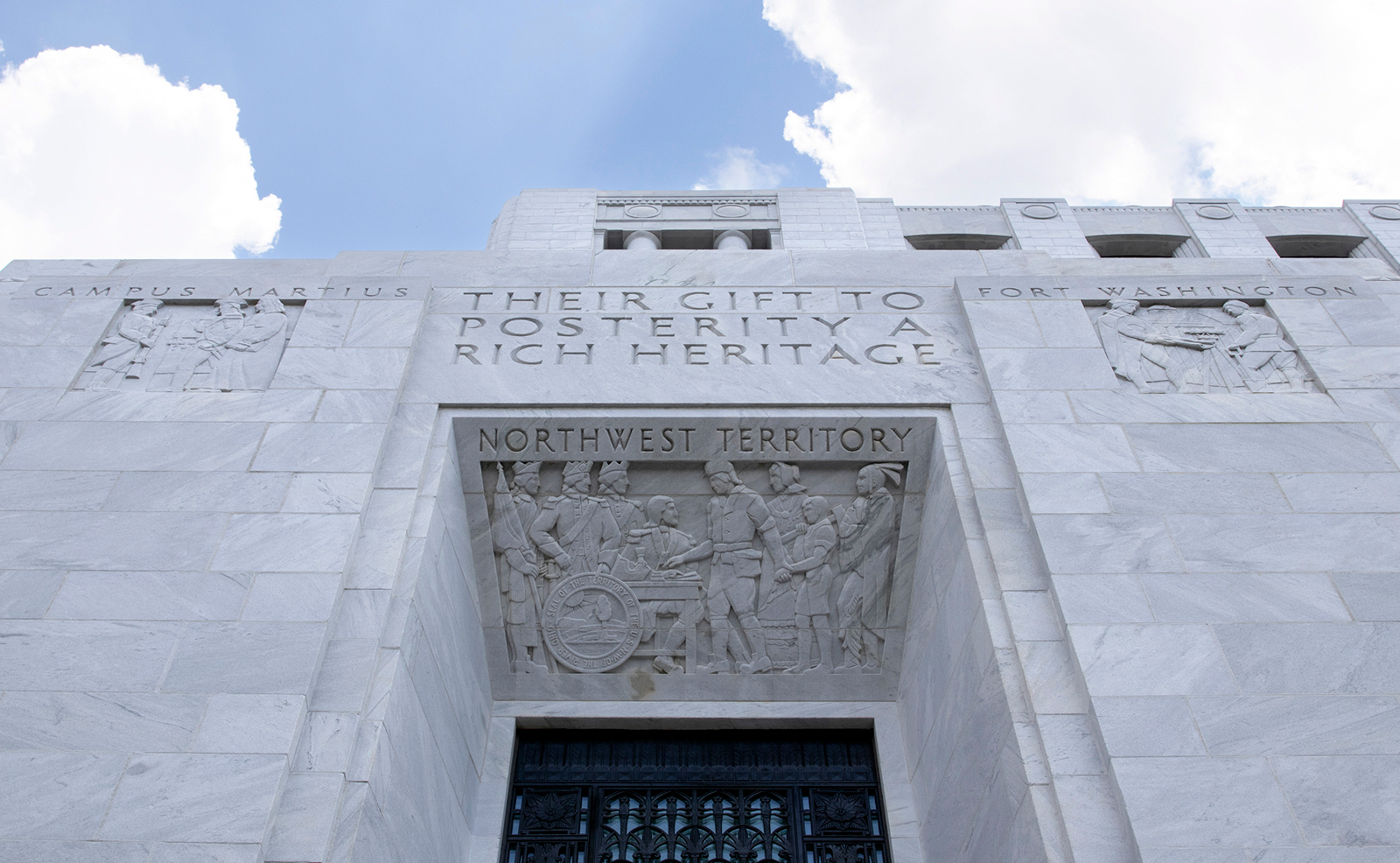 Image of an intricate carving of pioneers of the Northwest Territory; on either side are additional carvings depicting Campus Martius and Fort Washington