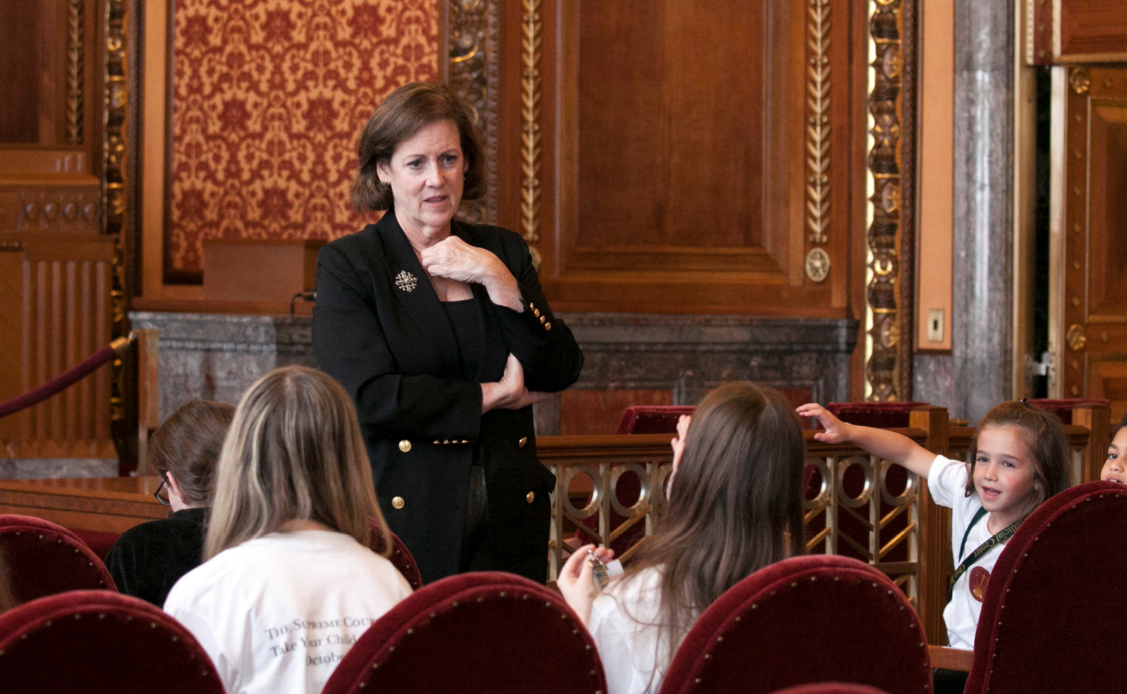 Image of a woman wearing a black suit speaking to a group of children in the courtroom of the Thomas J. Moyer Ohio Judicial Center