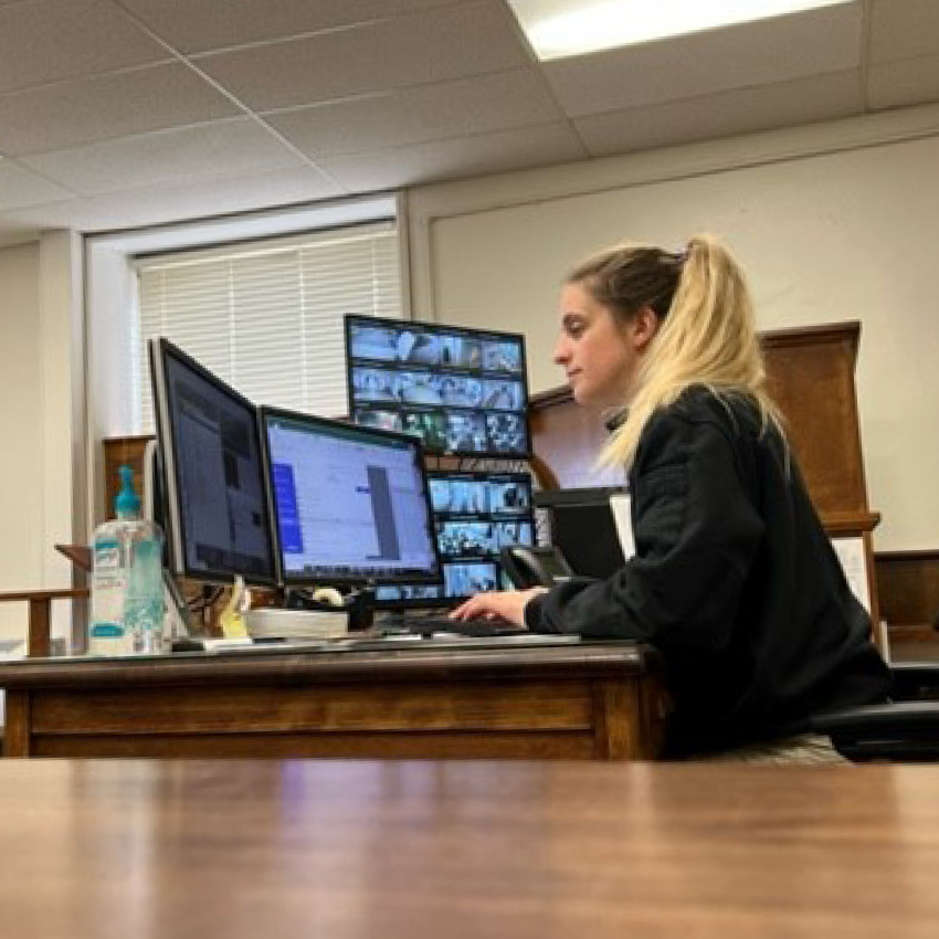 Image of a woman sitting at a desk with multiple computer monitors in front of her