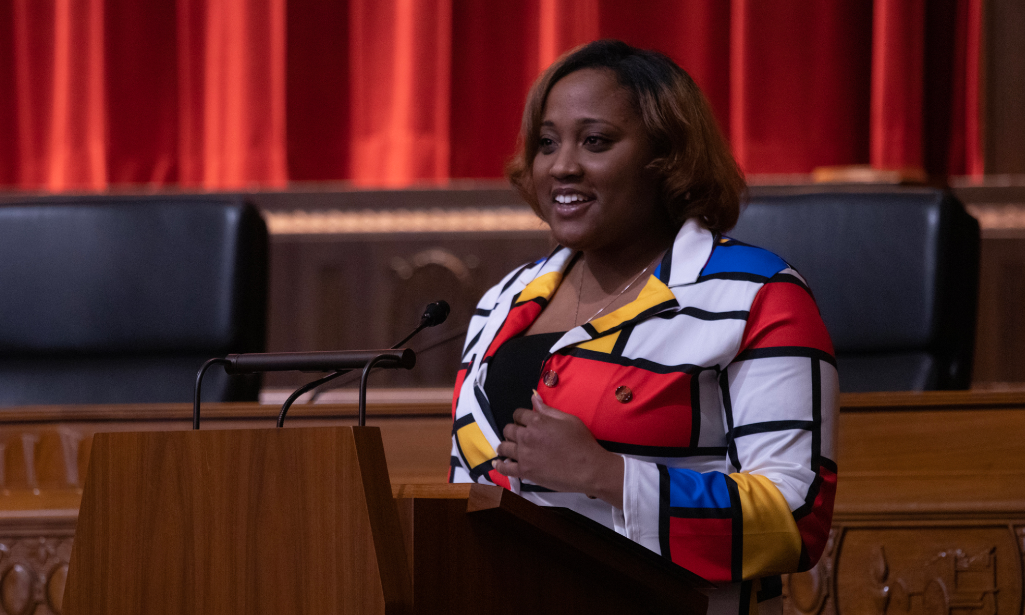 Image of a woman wearing a blouse with red, blue, and yellow blocks standing at a wooden podium in the courtroom of the Thomas J. Moyer Ohio Judicial Center.