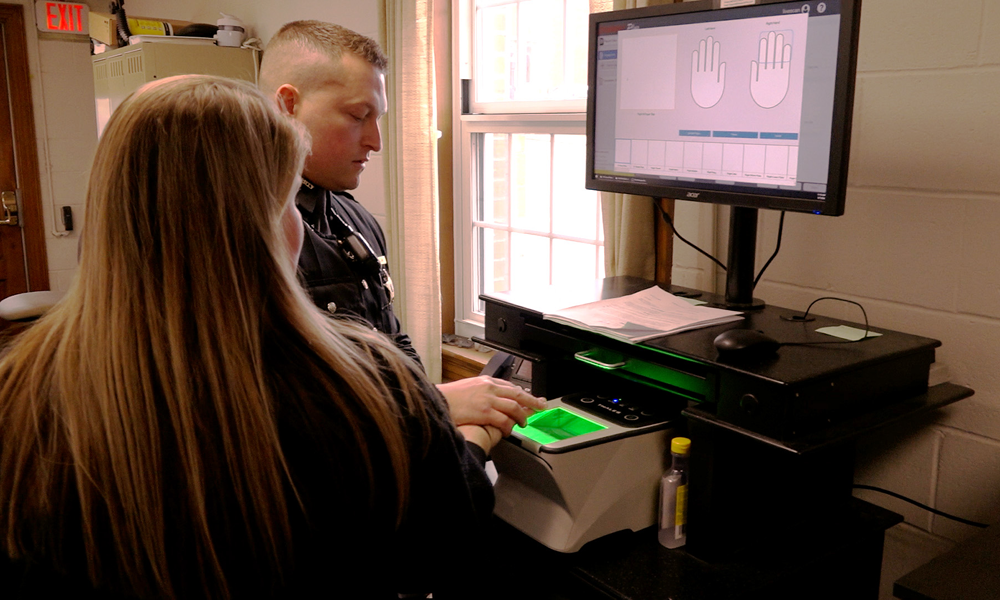 Image of a law enforcement officer fingerprinting a woman with long, hair.